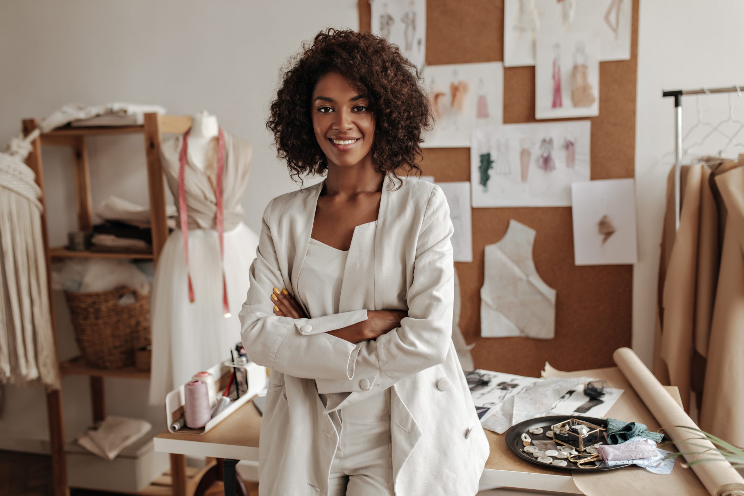 Home beautiful curly brunette dark skinned fashion designer poses in office, leans on table. young lady
